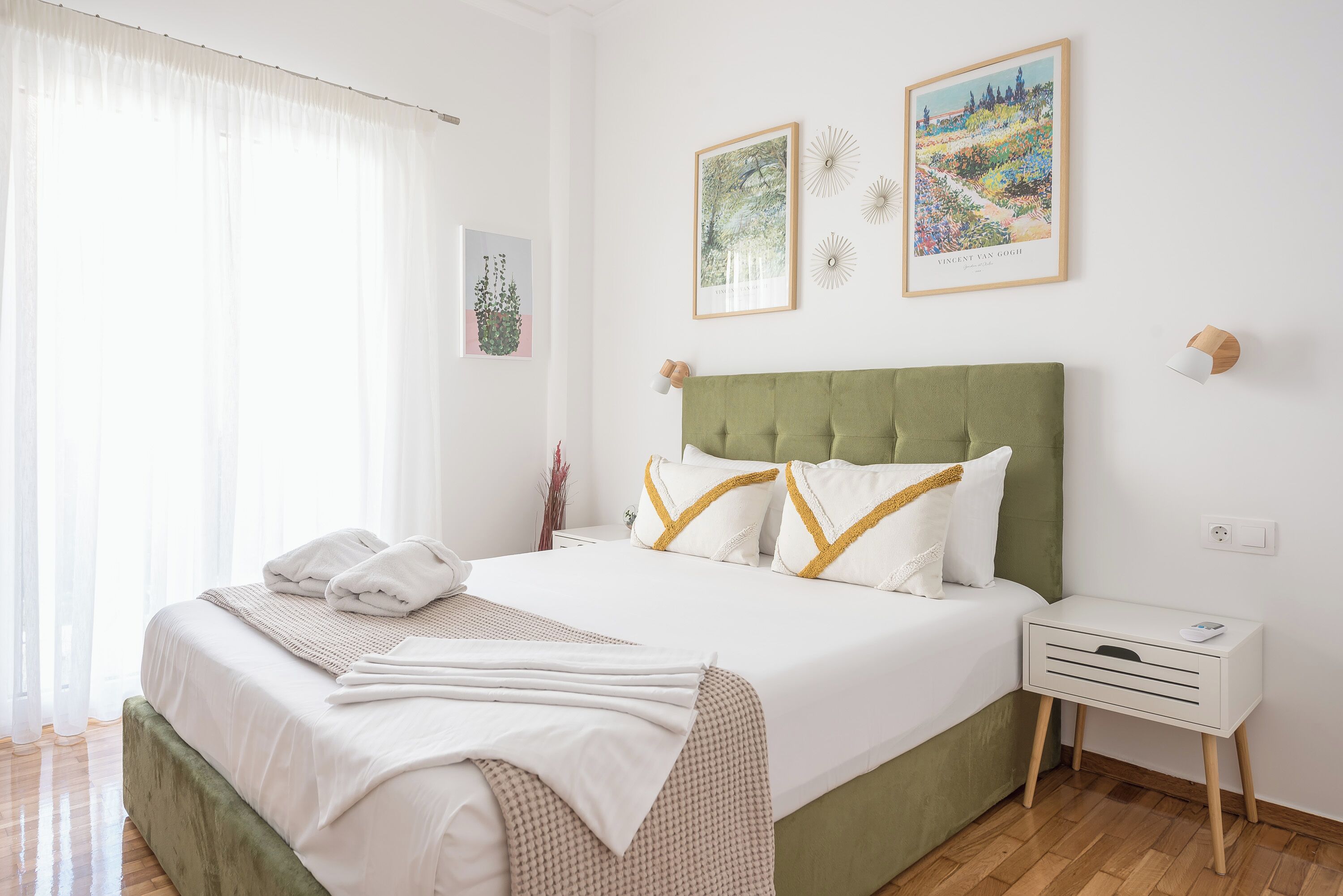 A neatly made bed with white linens and decorative pillows, a green upholstered headboard, and a bedside table with a lamp.