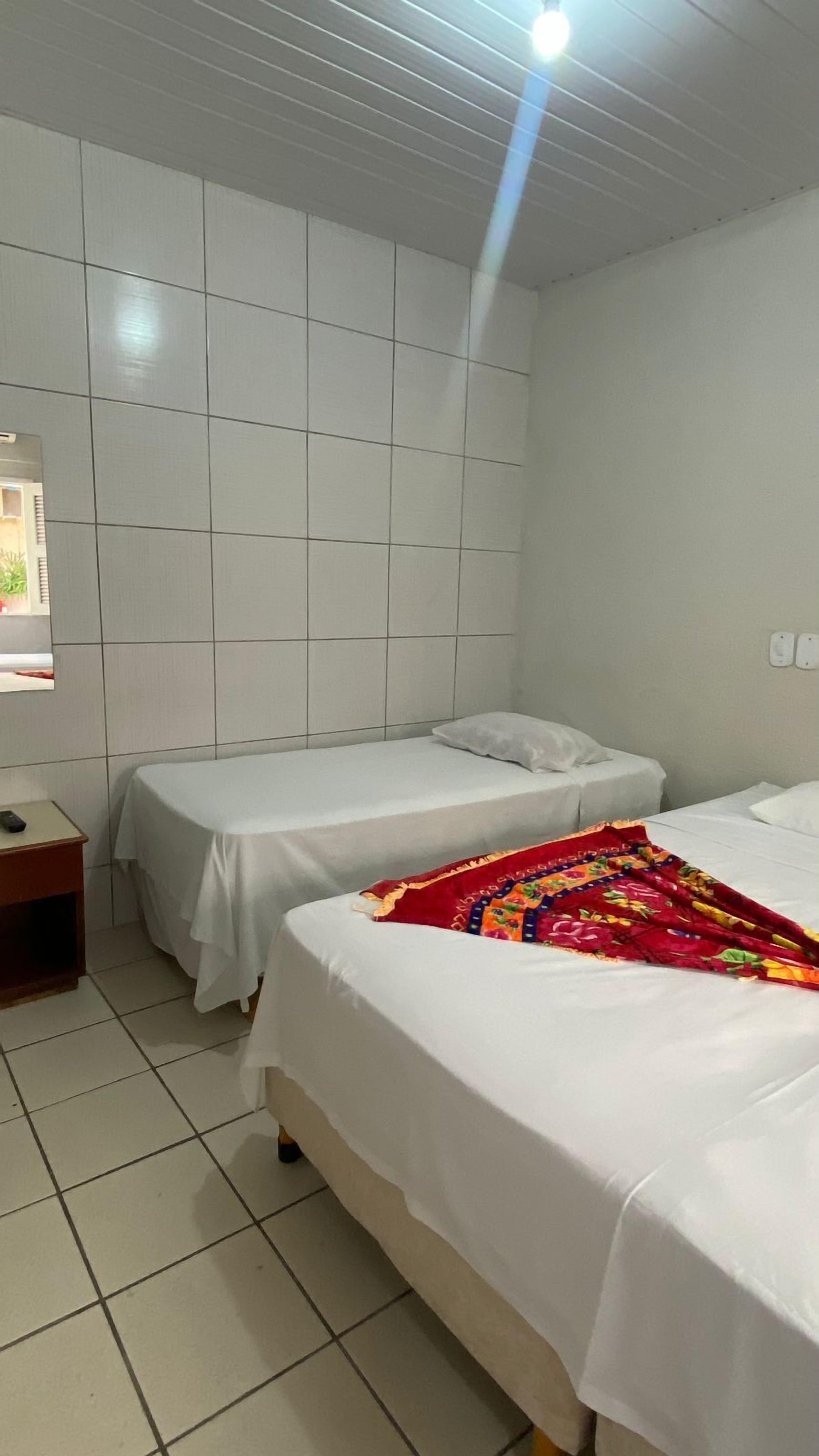 A hotel room with two single beds, a small bedside table, and a tiled floor.