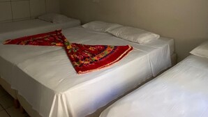 Et værelse med tre enkeltsenge, hver med et hvidt lagen og et farverigt tæppe. Der er en væghængt knagerække på højre side.