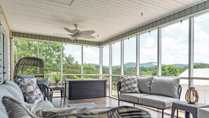A sunroom with a view of green hills, a ceiling fan, and a sofa with patterned cushions. - The Bell House - Contemporary Comfort Near Wards Road with a Luxurious Hot Tub! (Lynchburg)