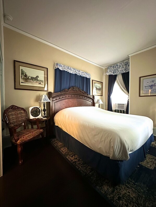 Ein Hotelzimmer mit einem großen Bett, einem Sessel, einem Nachttisch mit Lampe sowie zwei gerahmten Bildern an den Wänden.