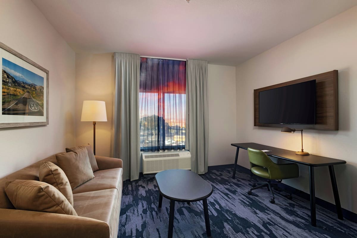 A hotel room with a sofa, a desk, a chair, a TV, and a window with curtains.