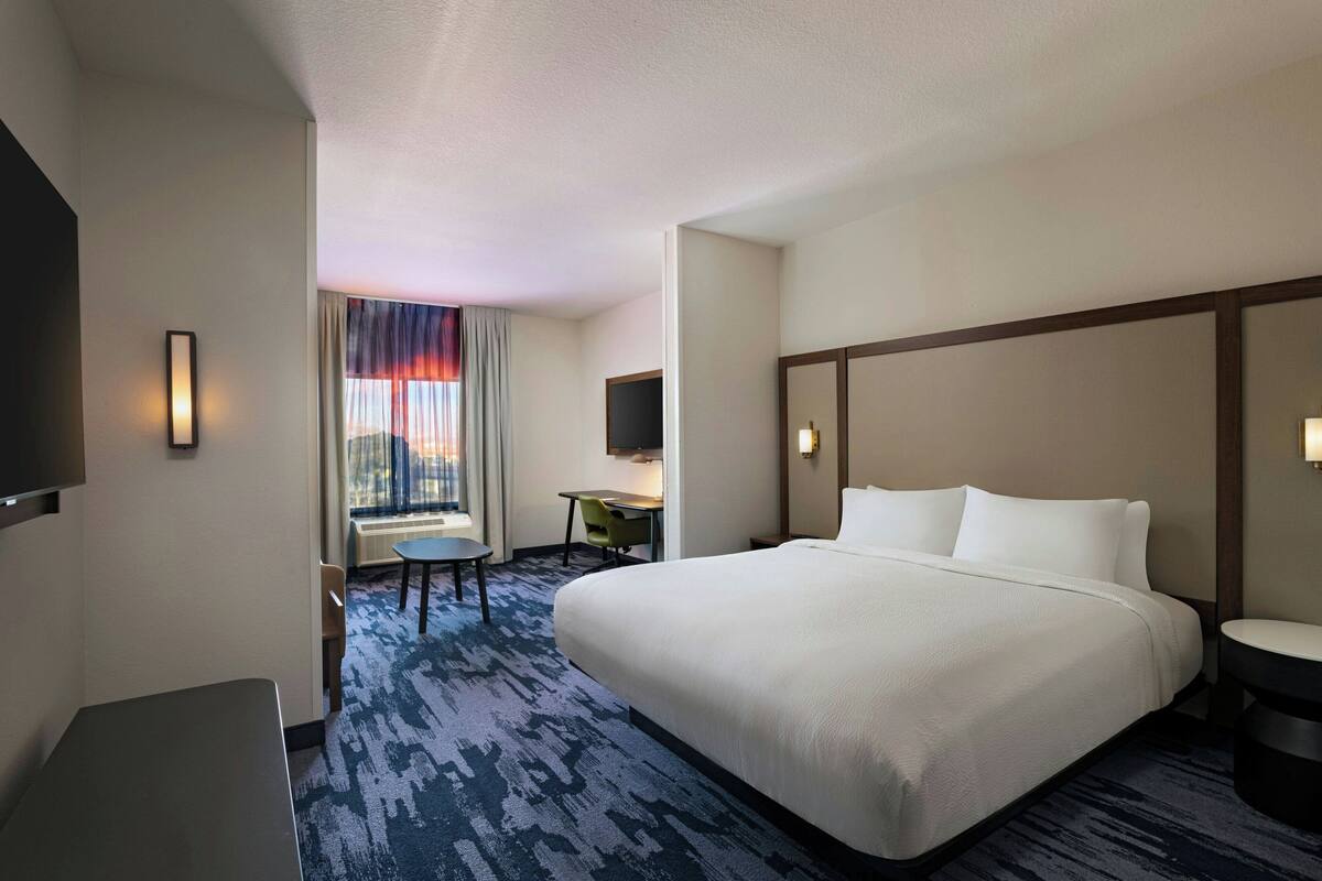 A hotel room with a large bed, a desk, a chair, and a TV.