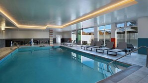 Piscina interna com água azul cristalina, rodeada por espreguiçadeiras e um design moderno no teto.
