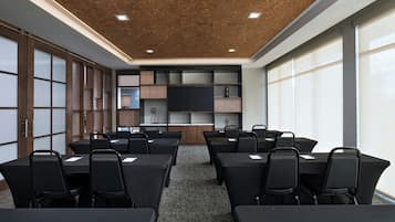 Une salle de conférence équipée de tables et de chaises, d’un grand écran et d’un plafond en bois.