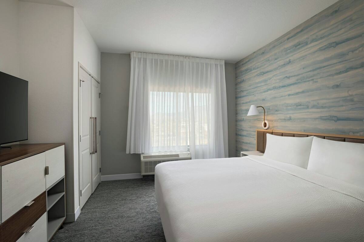 Une chambre d’hôtel avec un lit, une télévision, une armoire et une fenêtre avec des rideaux.