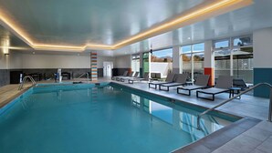 An indoor swimming pool with clear blue water, surrounded by lounge chairs and a modern ceiling design. - Towneplace Suites By Marriott Albuquerque Uptown (Albuquerque)