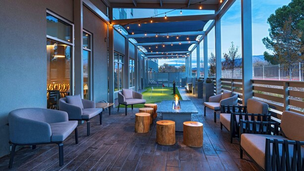 An outdoor patio area with seating and a fire feature, surrounded by a covered walkway and a view of a mountain. - Towneplace Suites By Marriott Albuquerque Uptown (Albuquerque)