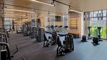 A modern gym with various exercise equipment, large windows, and a clean, spacious layout.