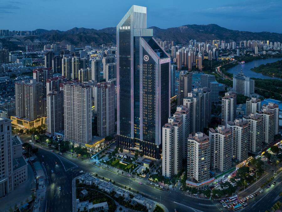 A high-rise building with a unique architectural design, surrounded by other tall buildings and a river in the background.