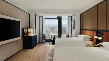 Habitación de hotel moderna con una cama grande, un escritorio con televisor, una mesita pequeña y vistas de la ciudad a través de amplios ventanales.