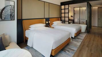 Habitación de hotel con dos camas, un espejo grande, una obra de arte colgada en la pared y un baño moderno visible a través de una puerta abierta.