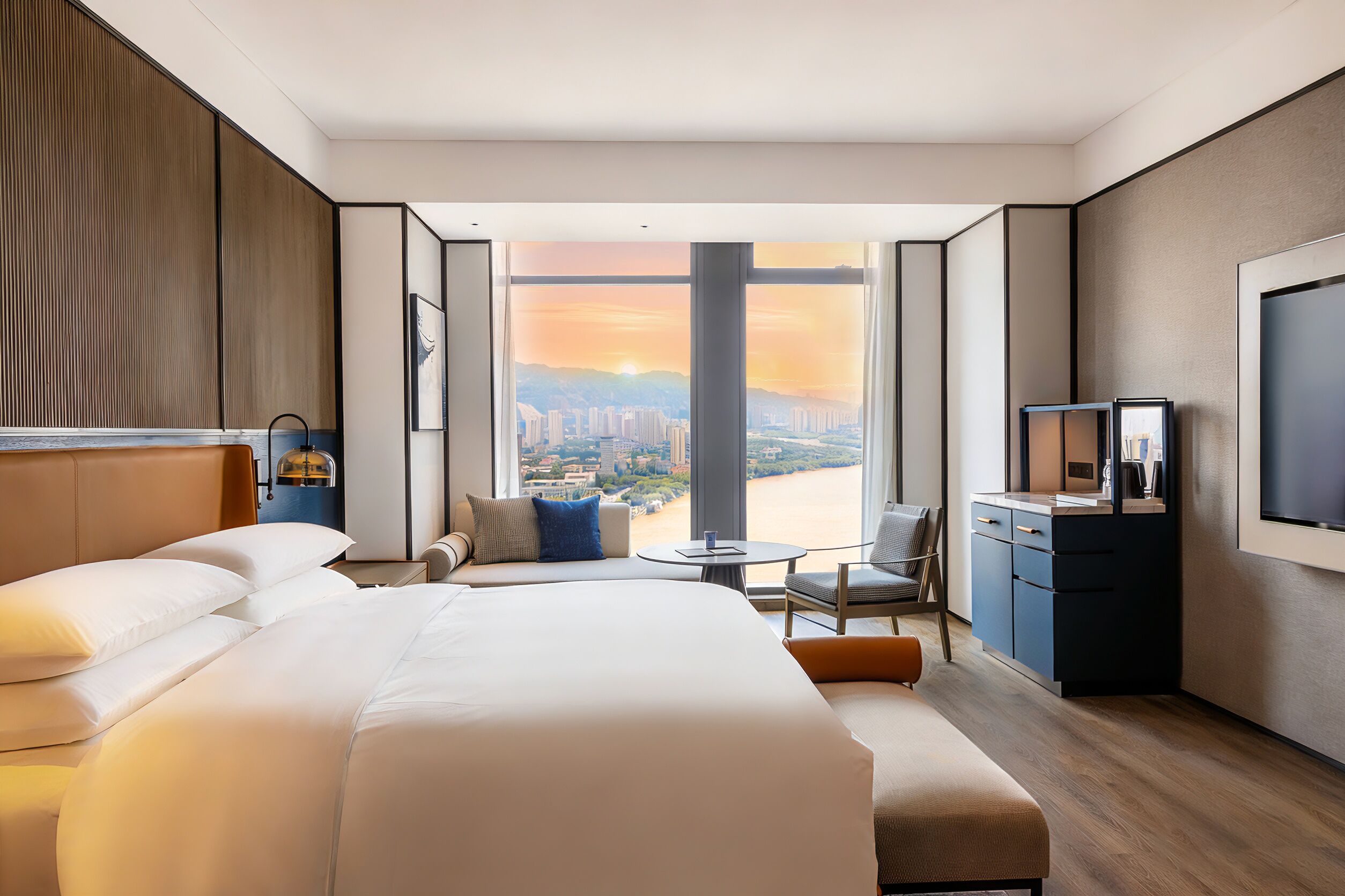 A hotel room with a large bed, a seating area, a TV, and a view of a cityscape.