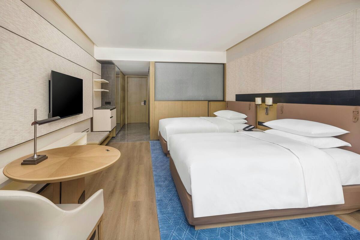 Quarto de hotel com uma cama grande, televisão, escrivaninha e área de estar.