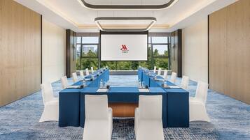 Een vergaderzaal met een lange tafel, witte stoelen en een groot scherm waarop het Marriott logo staat.