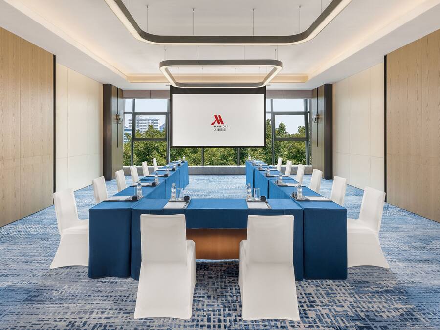 Een vergaderzaal met een lange tafel, witte stoelen en een groot scherm waarop het Marriott logo staat.