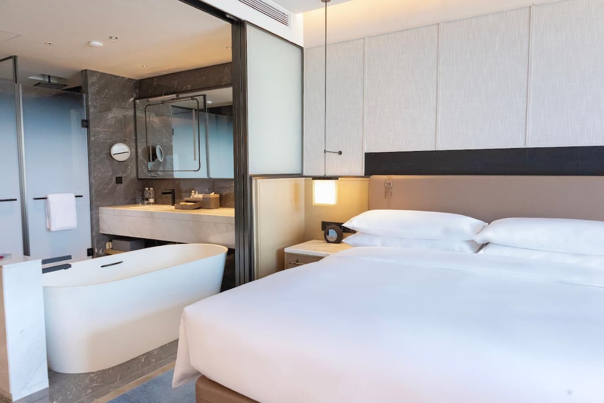 Quarto de hotel moderno com uma cama grande, área de estar separada, chuveiro embutido e toucador com espelho.