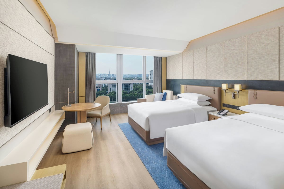 Quarto de hotel com duas camas, televisão, secretária e vista para a cidade.