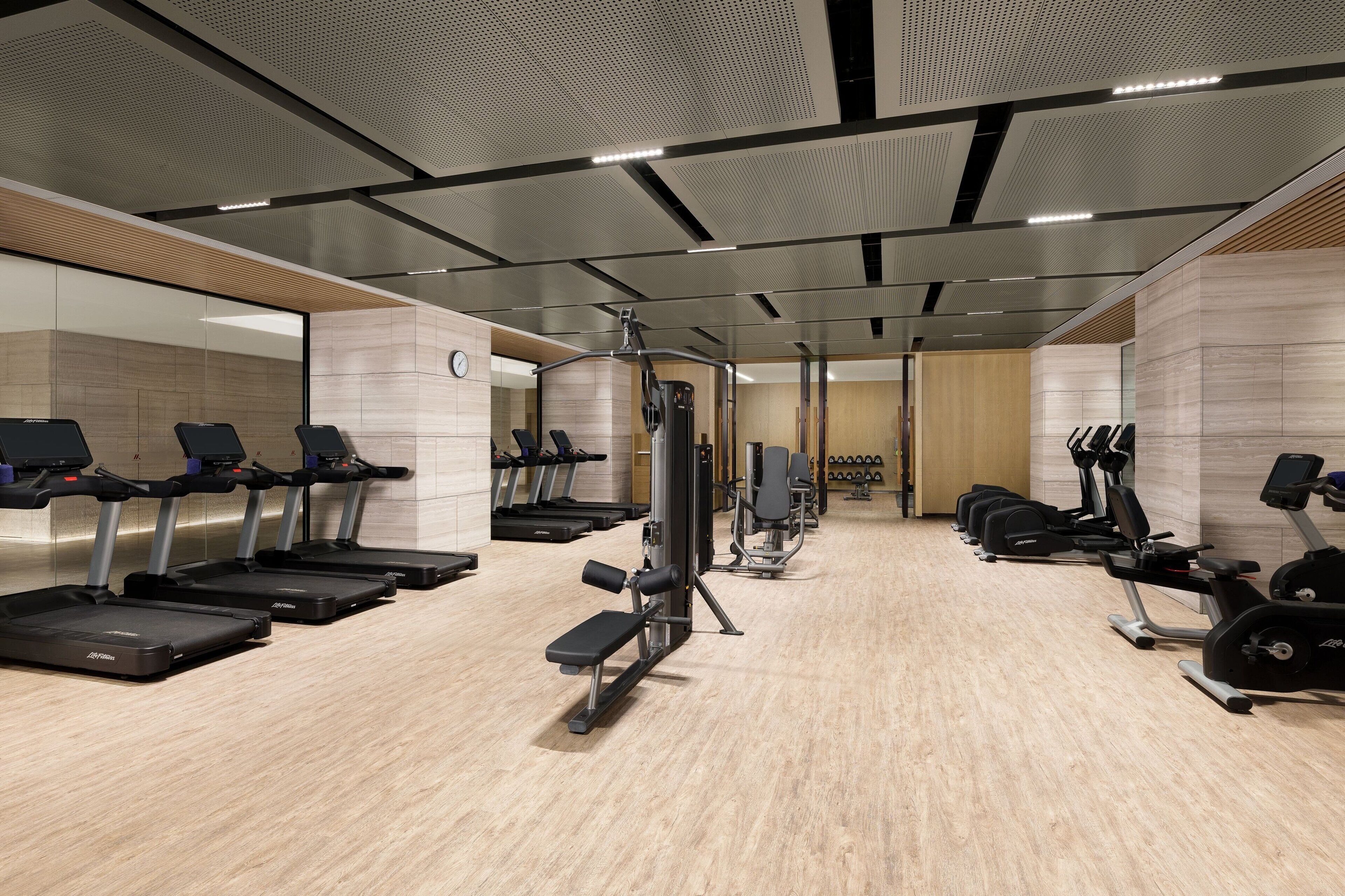 A modern gym with treadmills, elliptical machines, and weight stations.
