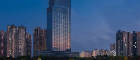 A high-rise hotel with a prominent logo at the top, surrounded by other tall buildings and a body of water in the foreground.