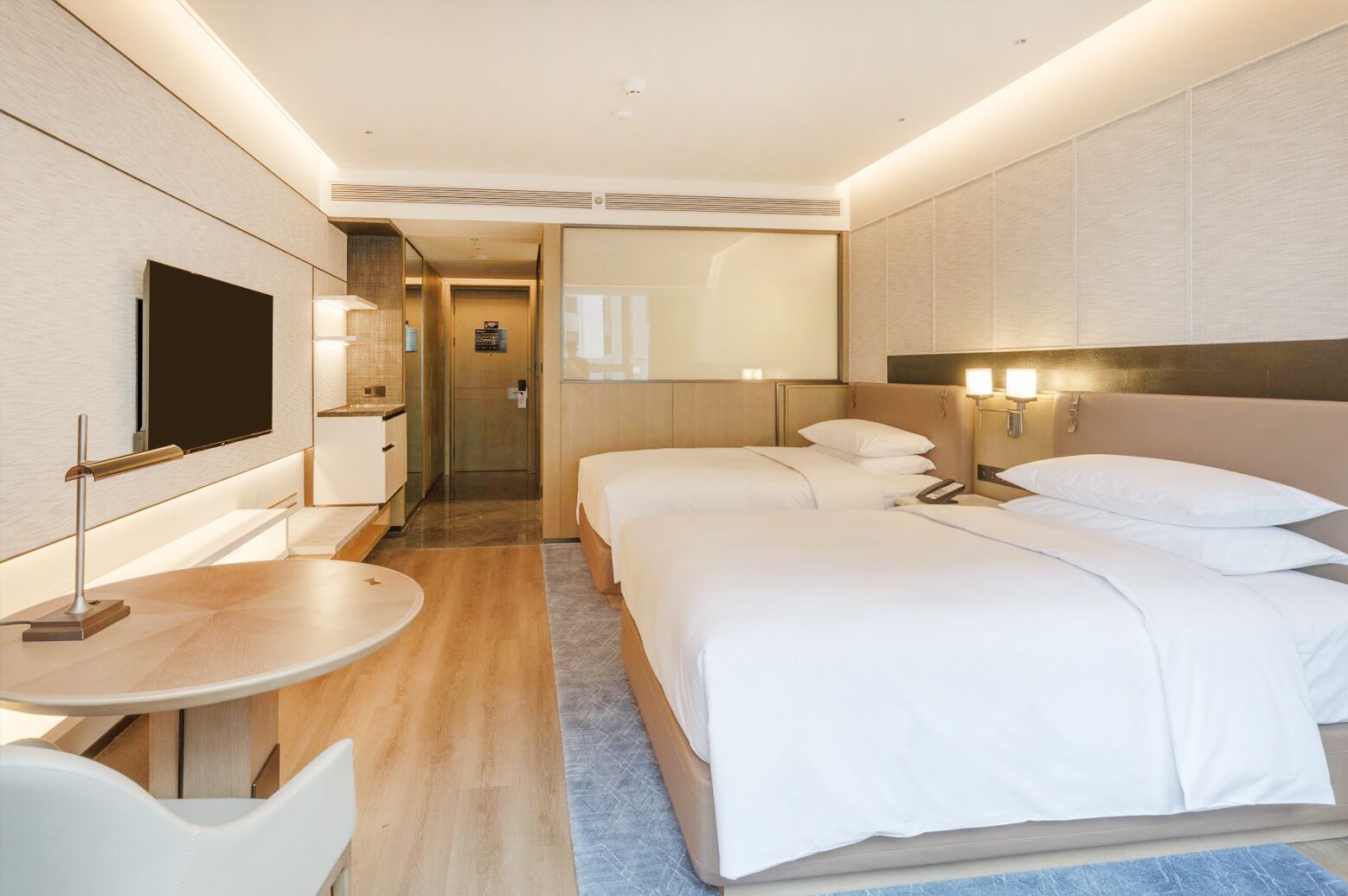 A modern hotel room with a flat-screen TV, a desk, two beds, and a bathroom visible through a door.