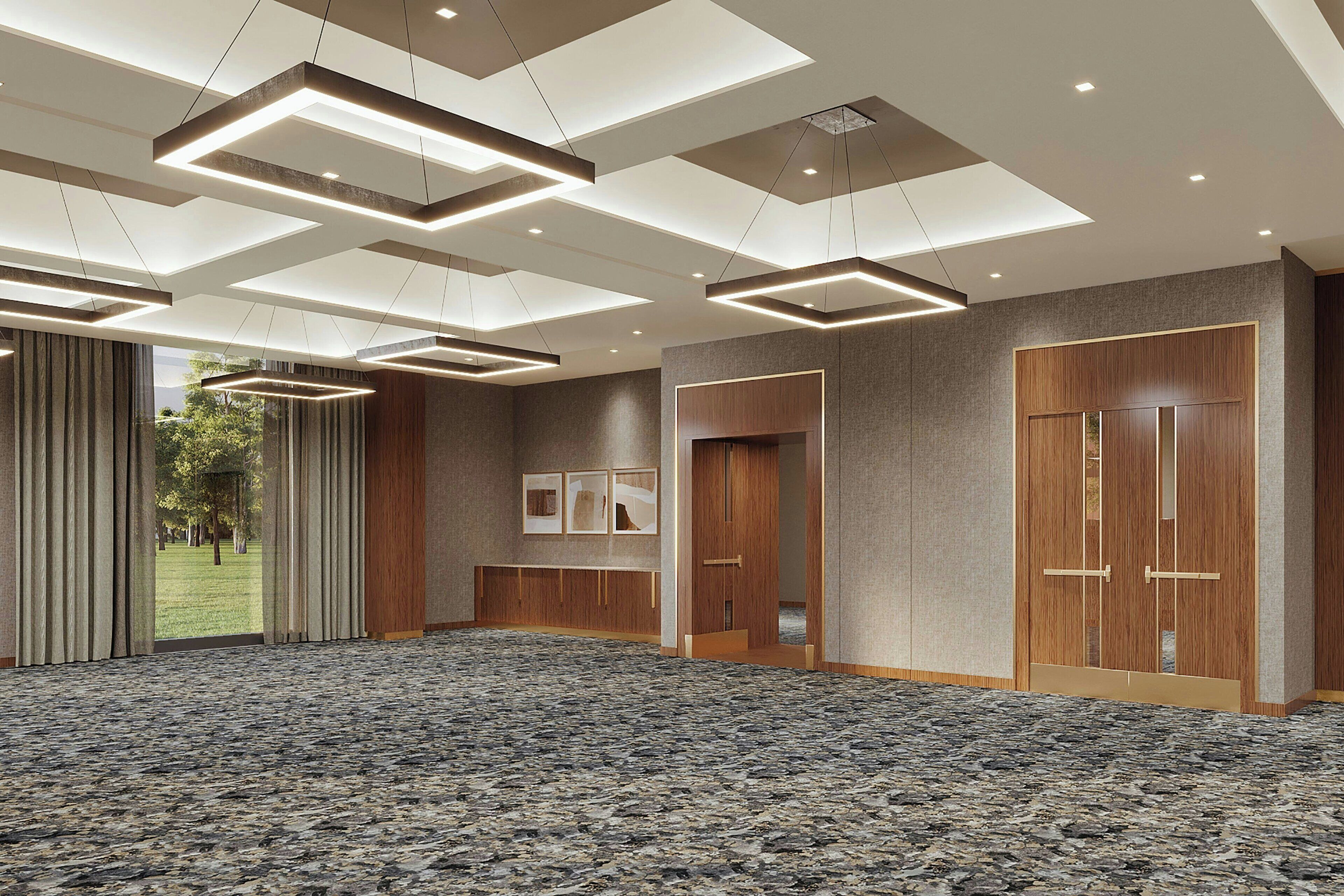 Una espaciosa sala de conferencias con alfombra estampada, luces empotradas en el techo, paneles de madera y puertas grandes.