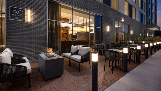 An outdoor seating area with wicker chairs and a fire feature, a brick wall, and a sign for AC Hotels Marriott. - AC Hotel By Marriott Newtown Square (Newtown Square)