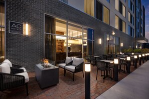 An outdoor seating area with wicker chairs and a fire feature, a brick wall, and a sign for AC Hotels Marriott. - AC Hotel By Marriott Newtown Square (Newtown Square)