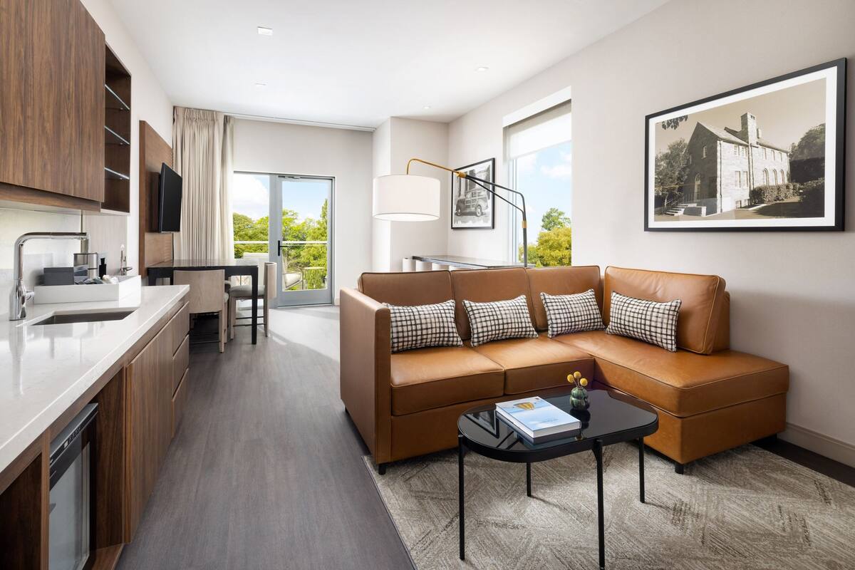 A modern living room with a brown sofa, a coffee table, and a kitchen area with a sink and cabinets.
