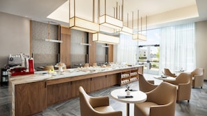 A modern kitchen with a central island, wooden cabinets, and a seating area with round tables and chairs. - AC Hotel By Marriott Newtown Square (Newtown Square)