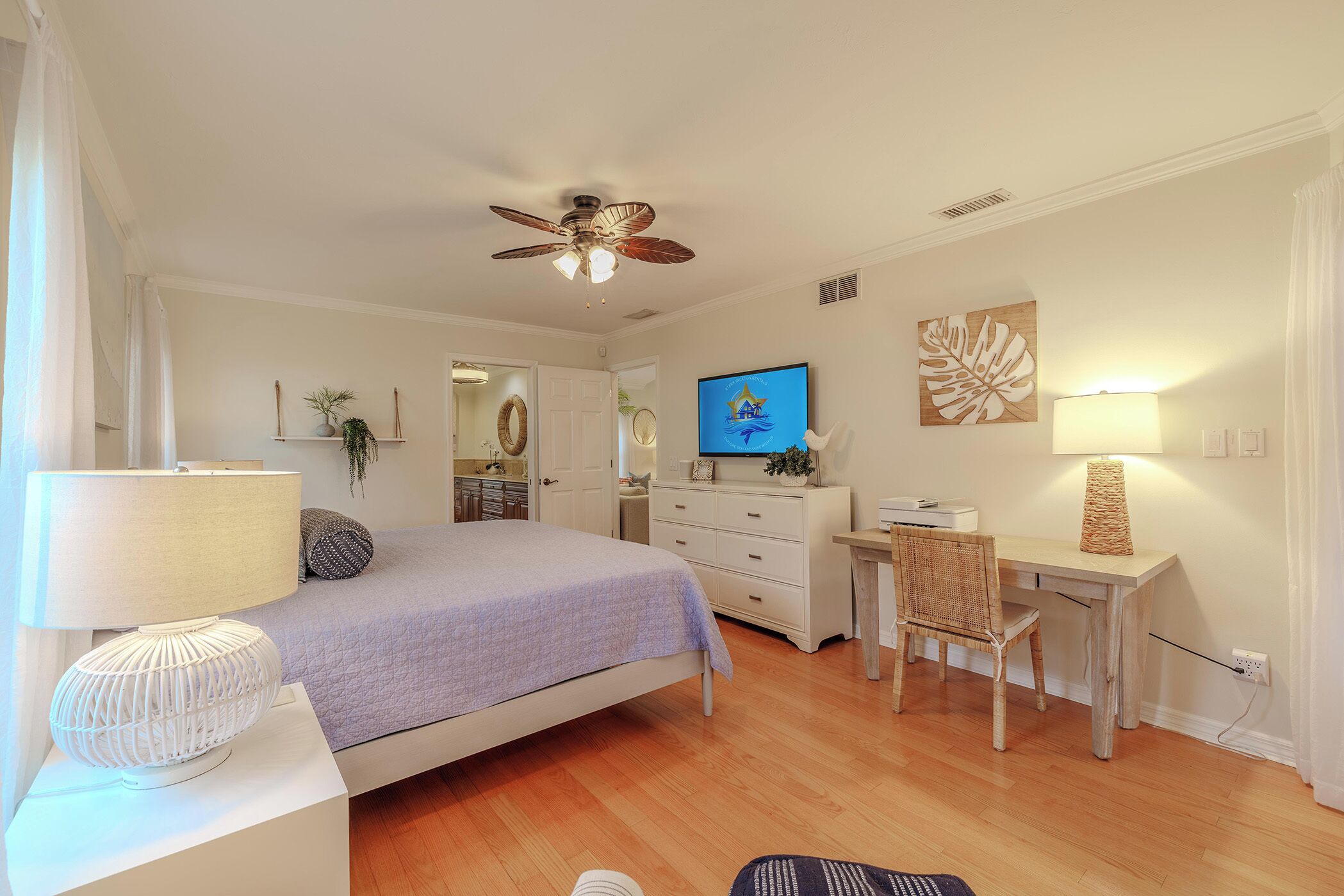 Un dormitorio con cama, escritorio, silla, televisor y ventilador de techo.