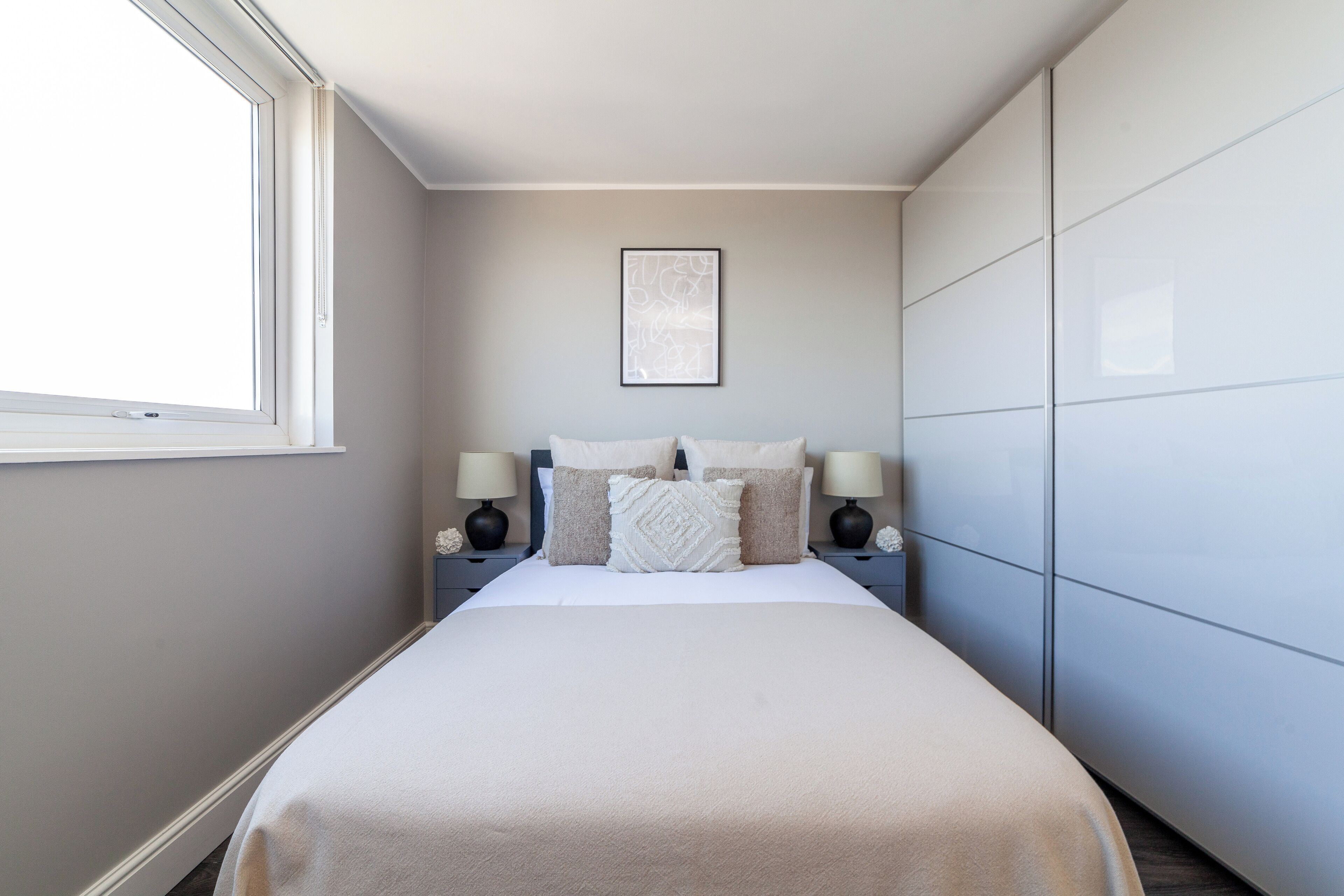 A bedroom with a bed, two bedside tables with lamps, a window, and a wardrobe.