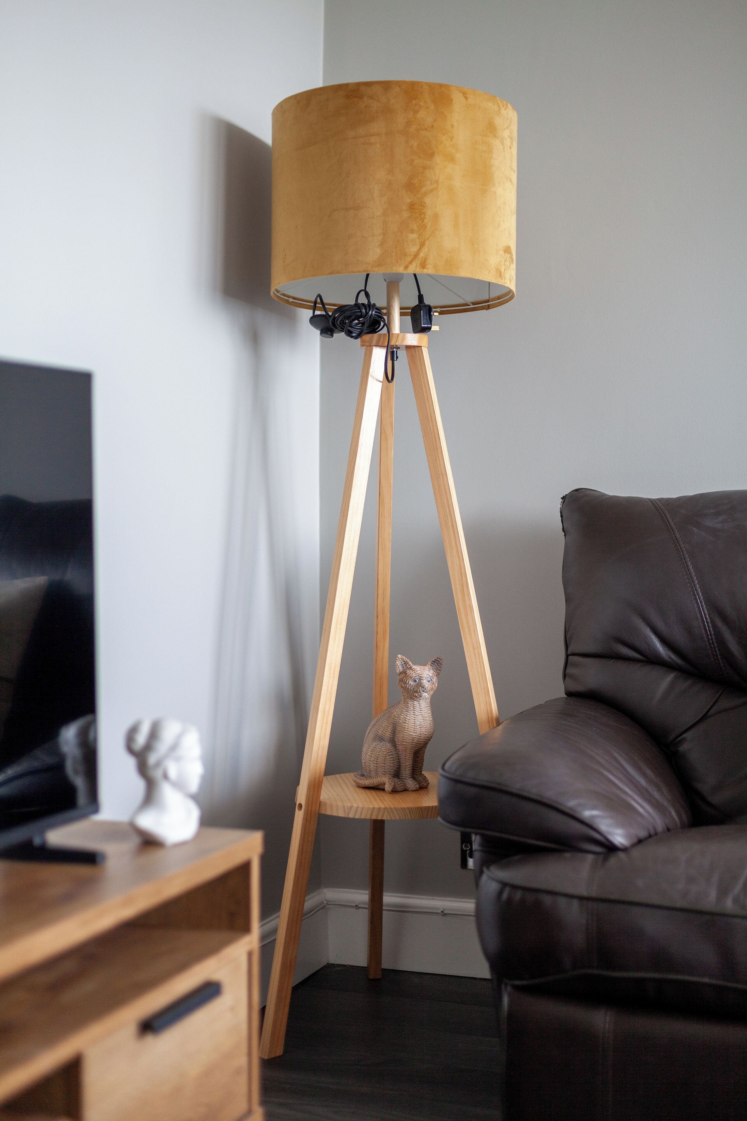 En moderne stue med en gulvlampe i træ, en lædersofa og et lille træbord med en skulptur.