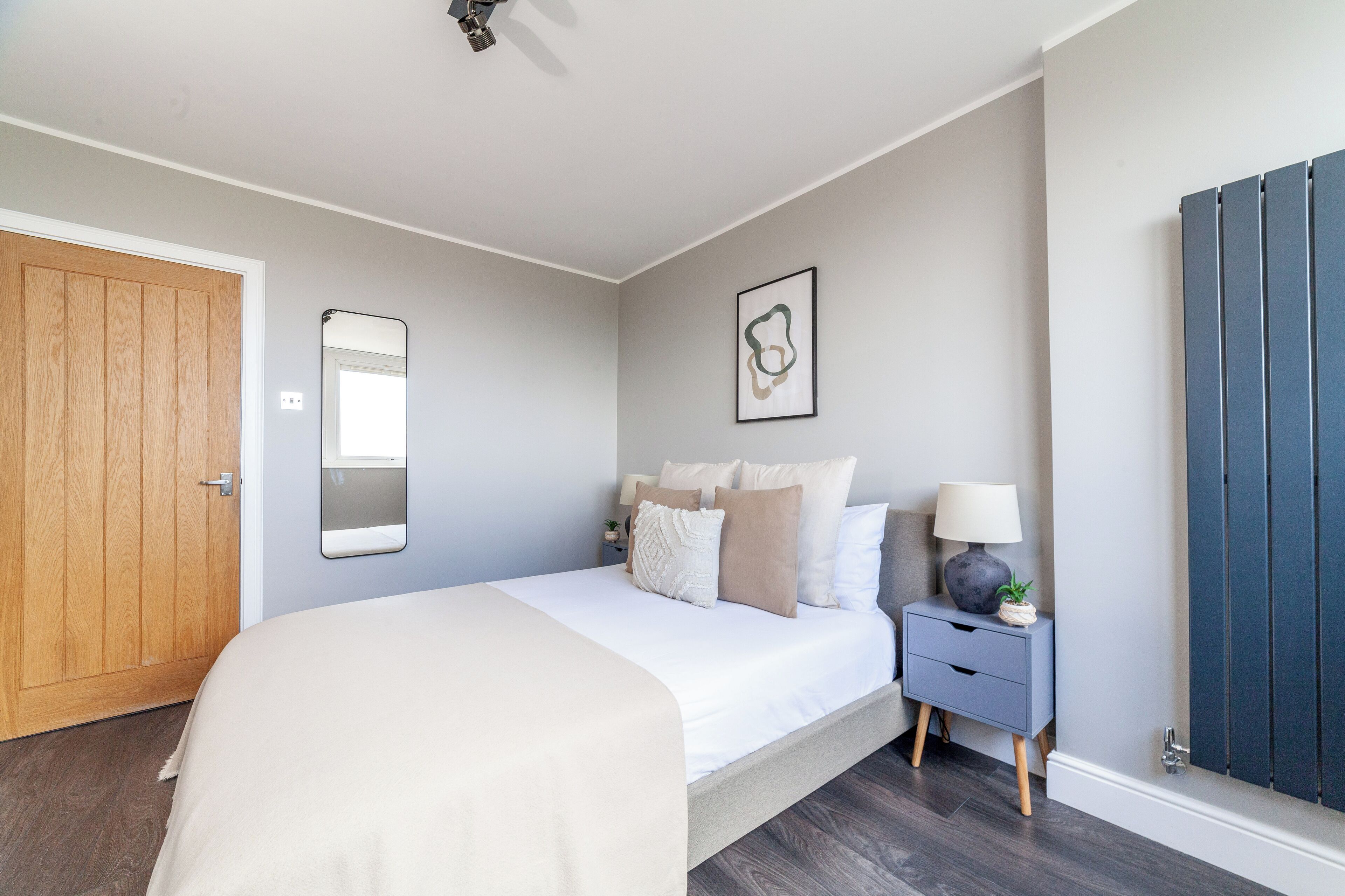 Un dormitorio con cama, mesita de noche, lámpara y un espejo en la pared.