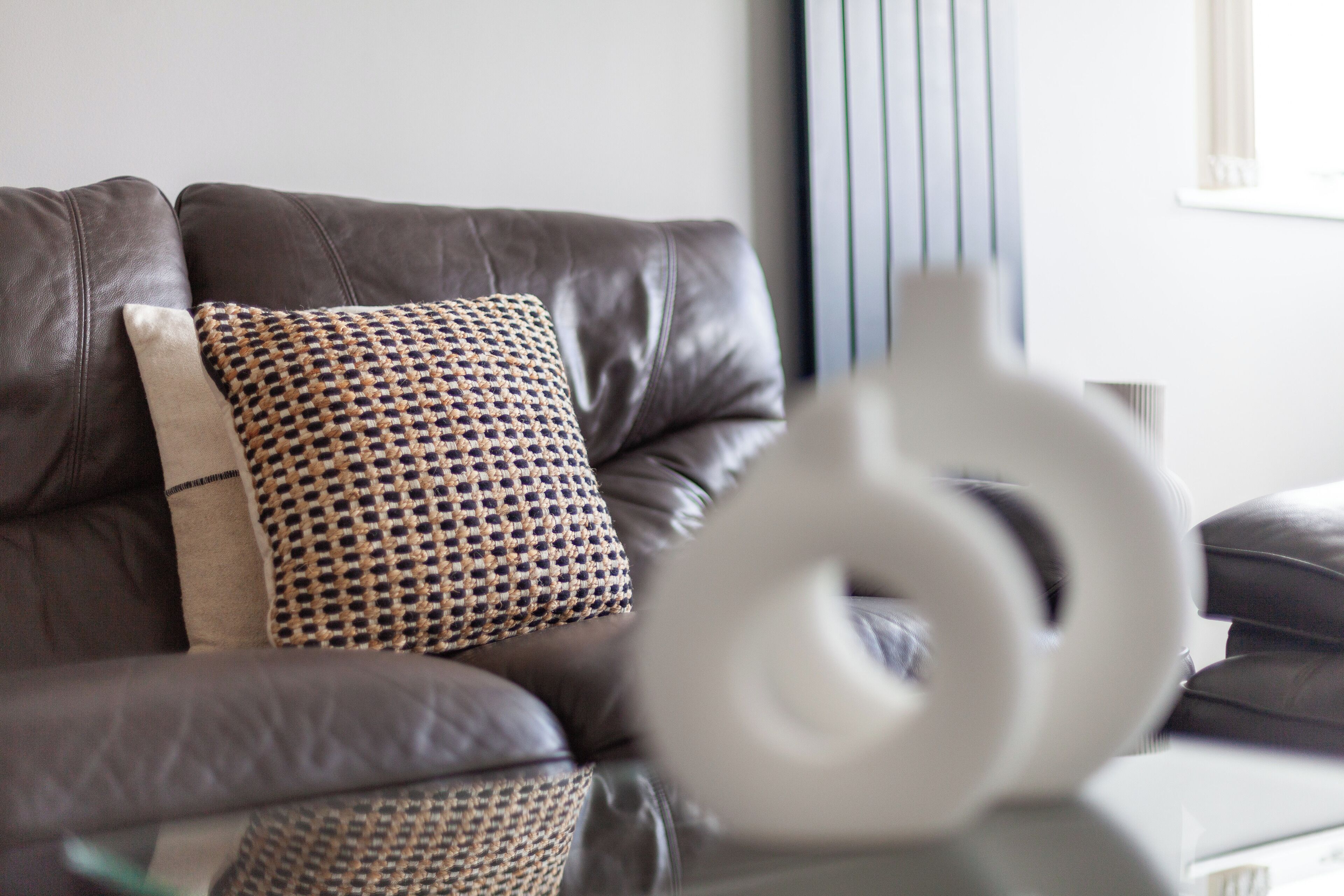 A brown leather sofa with a patterned cushion and a white abstract sculpture on a reflective surface.