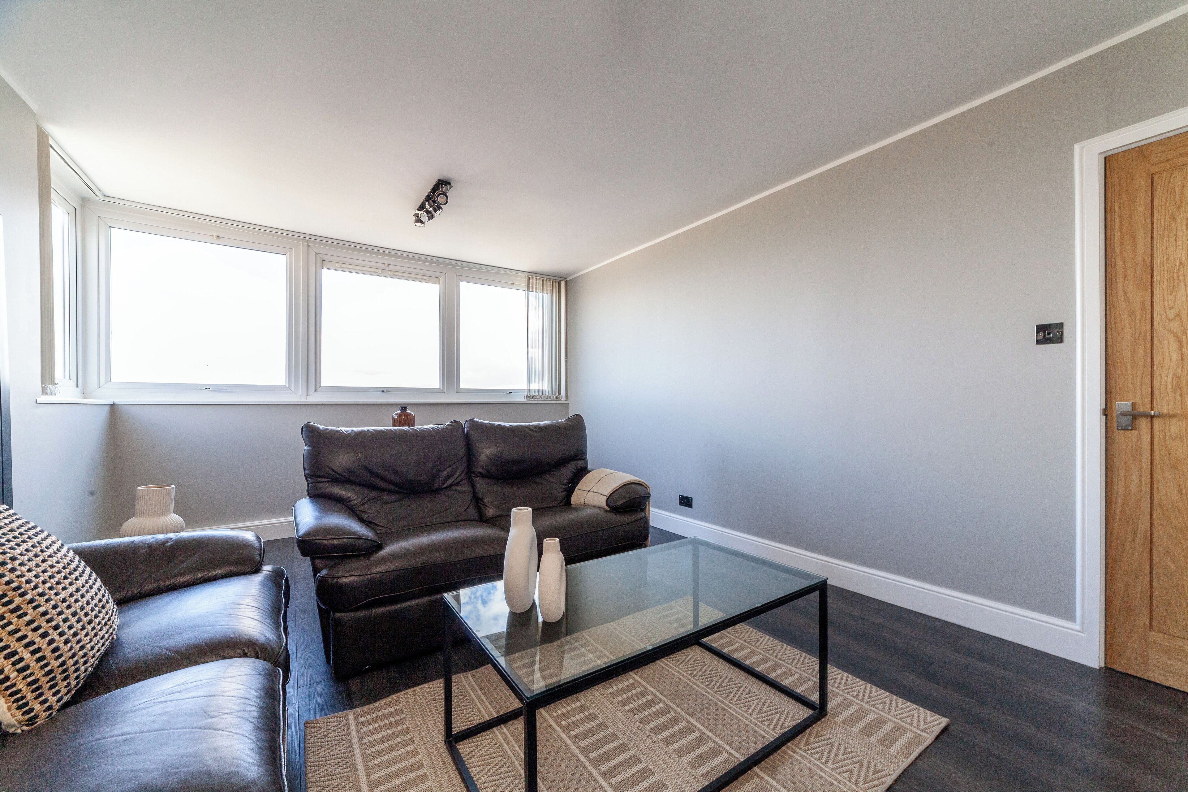 A modern living room with a dark leather sofa, a glass coffee table, and a patterned rug.