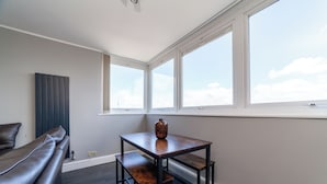A modern room with a dark wood table and bench, a dark leather sofa, and a large window with a view of the sky. - The Old Street Luxury Apartment (London)