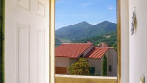 A doorway leading to a balcony with a view of a mountain and red-roofed buildings. - Le Nid de Gilles (Collioure)