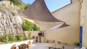 An outdoor patio with a table, chairs, a barbecue grill, and a shade sail. - Le Nid de Gilles (Collioure)