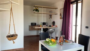 Un comedor con una mesa blanca, sillas y una cesta colgante. Hay estantes sobre la mesa con diversos objetos.