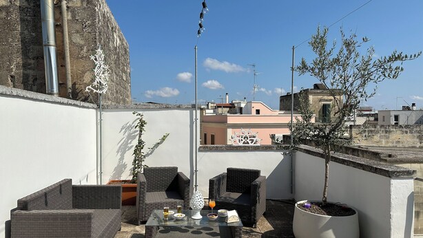 Una terraza en la azotea con mobiliario de mimbre, una mesa con bebidas y una planta en maceta.