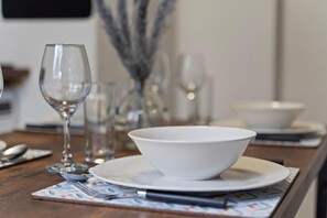 Une table à manger avec un bol blanc posé sur une assiette, entourée de verres transparents et de couverts.