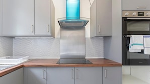 Cozinha com armários cinzas, coifa de aço inoxidável e painel de azulejos.