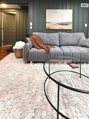 A living room with a grey sofa, a white shaggy rug, a coffee table, and a painting on the wall.