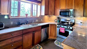 A kitchen with wooden cabinets, a stainless steel stove, and a microwave. - Sweet Seco Casita is a classic Taos Adobe Home (Arroyo Seco)