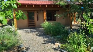 A rustic building with a red roof, a wooden door, and a gravel pathway leading to it. - Sweet Seco Casita is a classic Taos Adobe Home (Arroyo Seco)