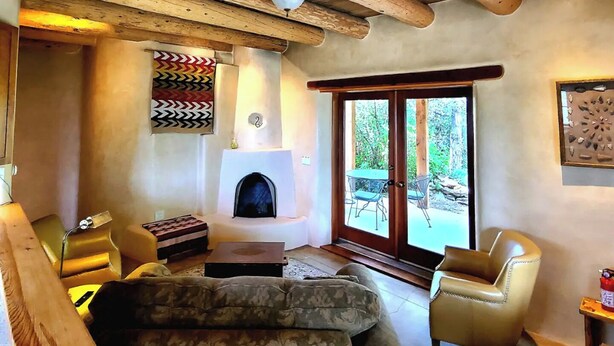 A cozy living room with a fireplace, wooden ceiling beams, and a view through the glass doors. - Sweet Seco Casita is a classic Taos Adobe Home (Arroyo Seco)