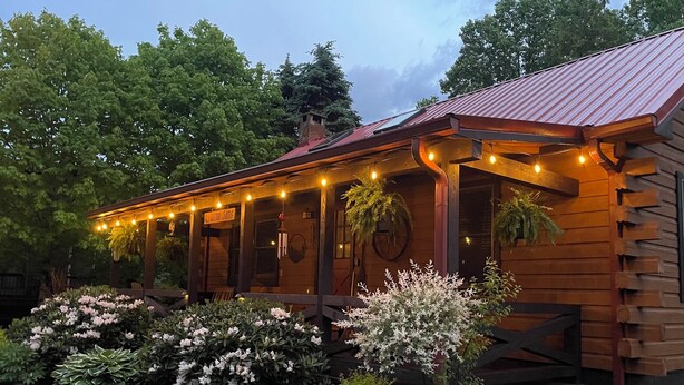 Una caba ña de madera con porche, luces de cuerda e incluso plantas en macetas.