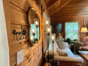 L’intérieur d’un chalet accueillant, avec des murs en bois, un canapé blanc, une petite table et des luminaires fixés au mur.