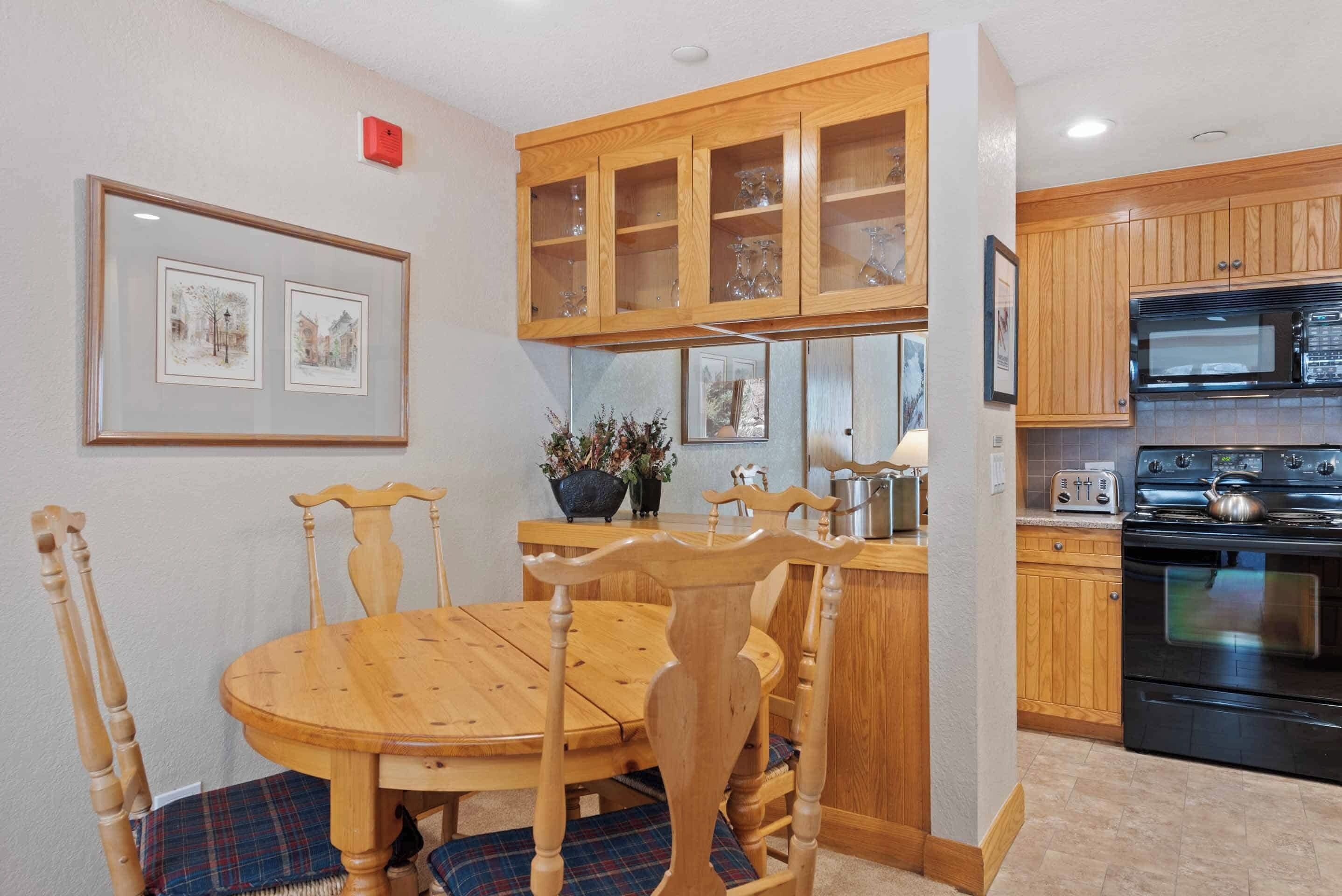 Un comedor con una mesa y sillas de madera, una cocina con armarios y electrodomésticos de madera, y cuadros en la pared.